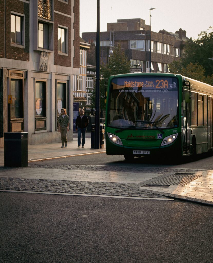Green single-decker bus passing through a Kent town centre street