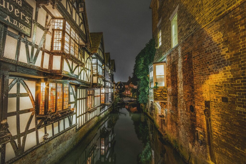 Historic timber-framed buildings lit up at night alongside a narrow river in a Kent town