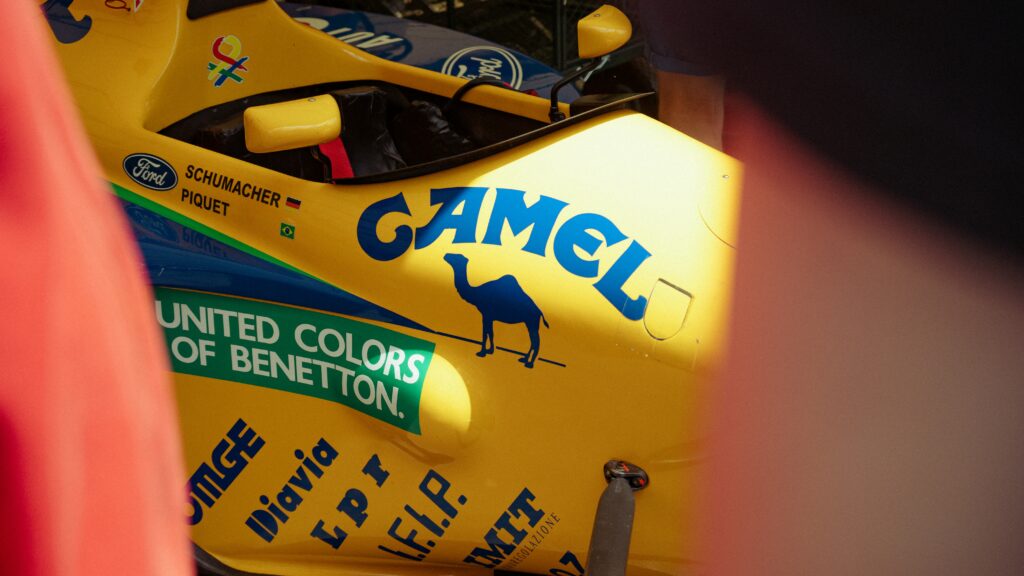 Side of a vintage yellow Benetton Formula One car carrying Camel, Ford and United Colors of Benetton sponsor branding